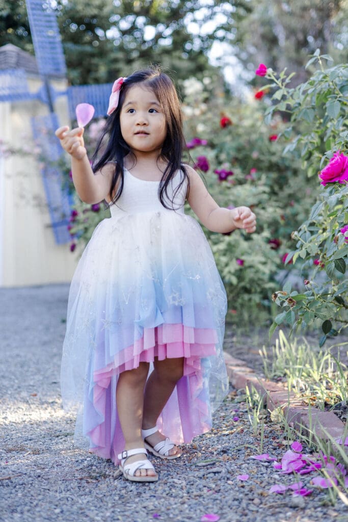 A young girl wearing a beautiful flowy dress holds a fallen rose petal in the rose garden at Fremont during a family photoshoot