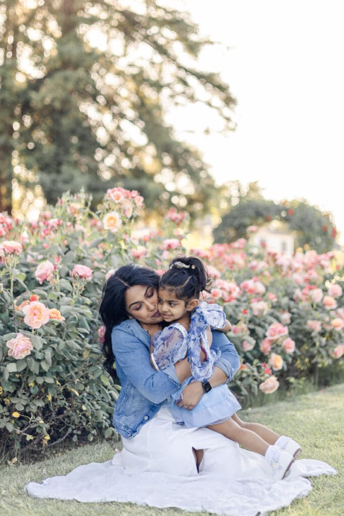 Mom and her toddler daughter lovingly hug each other during their photoshoot in the blooming rose garden in San Jose