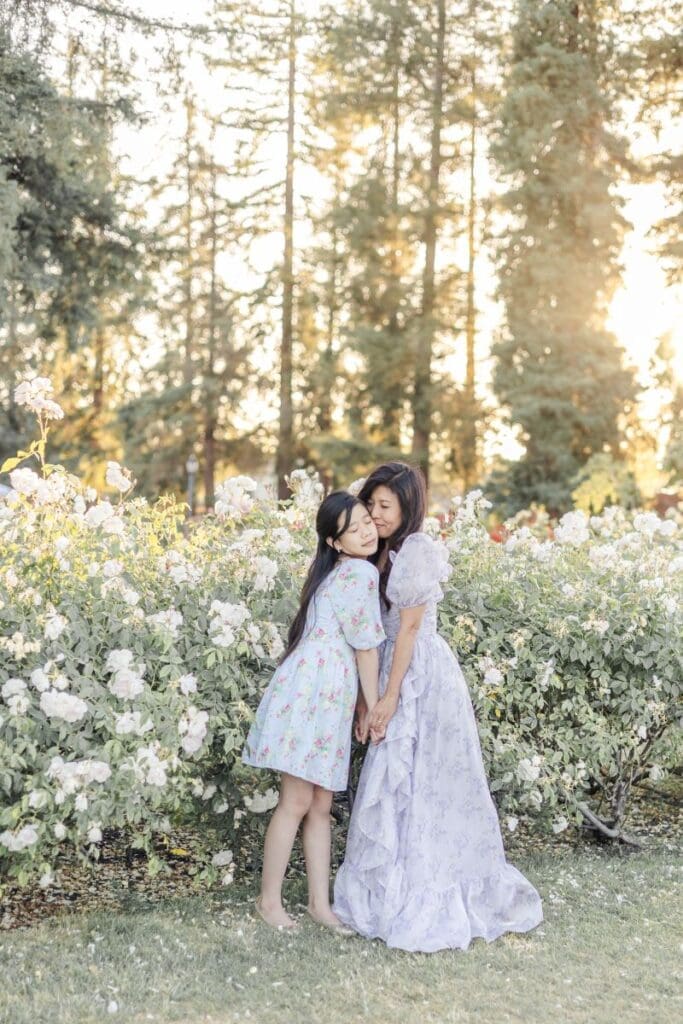 Mom and teenage daughter share a sweet moment with mom placing a soft kiss on her daughters cheeks during a sunset photoshoot at the rose garden in San Jose