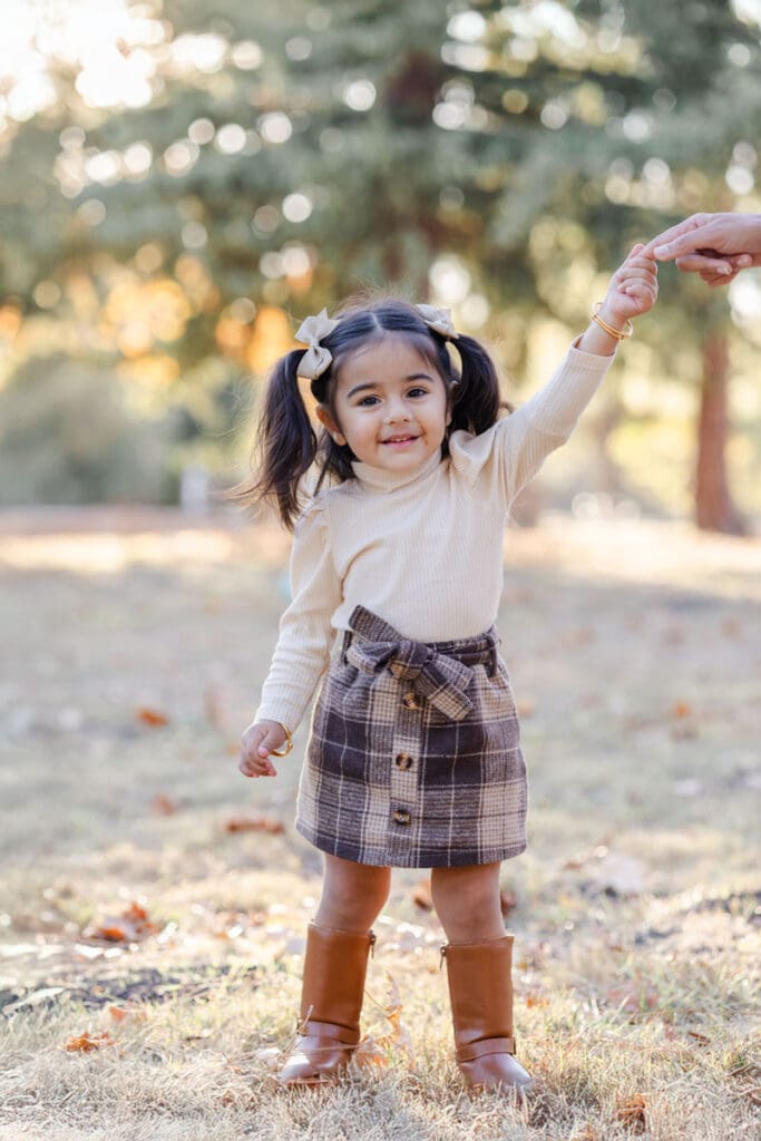 Toddler daughter holding her moms hand and smiling at the camera during a fall family photoshoot 
