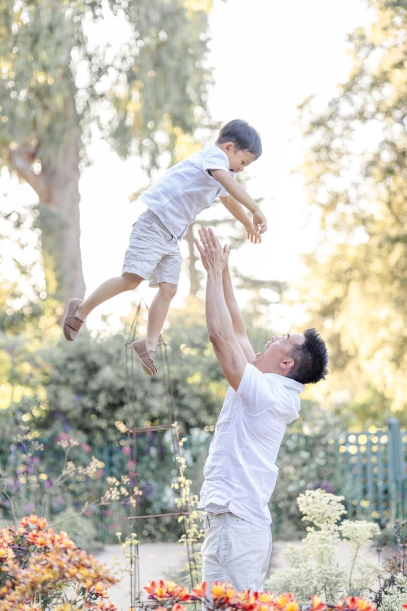 Dad lifts toddler boy into the air during a playful moment captured during a spring garden photoshoot