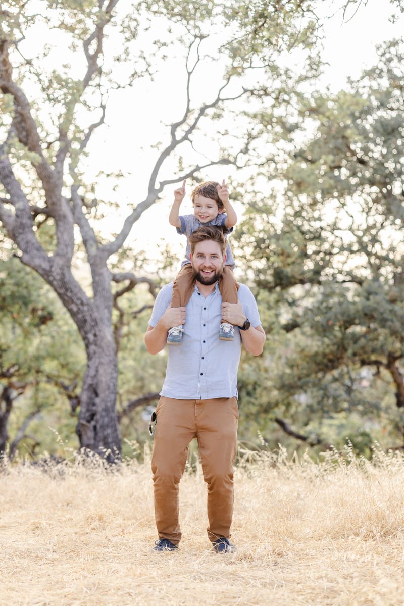 Dad lifts toddler boy onto his shoulders during a playful moment captured during a fall family photoshoot